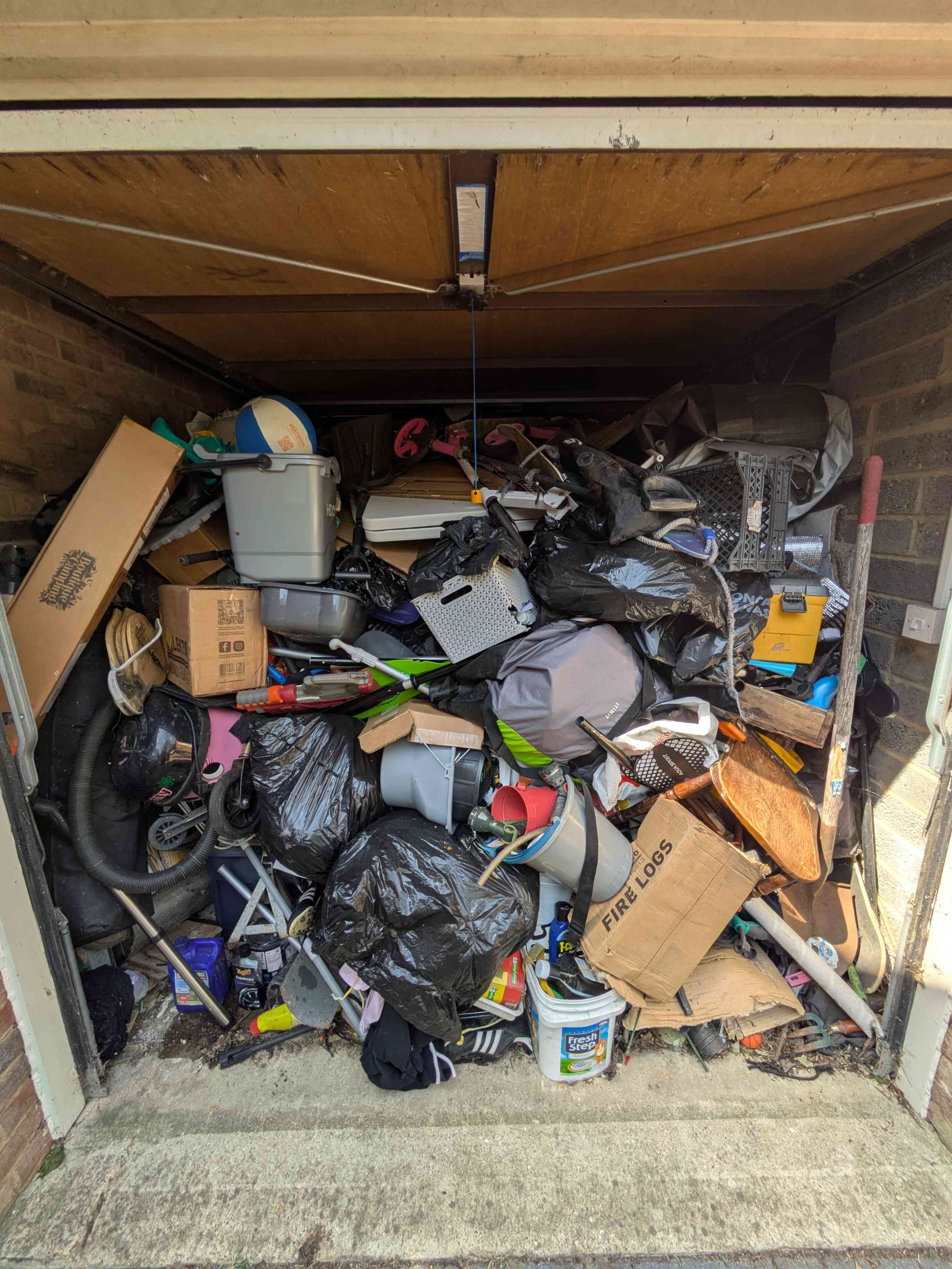 A single garage stacked from floor to ceiling with bin bags, boxes and household clutter