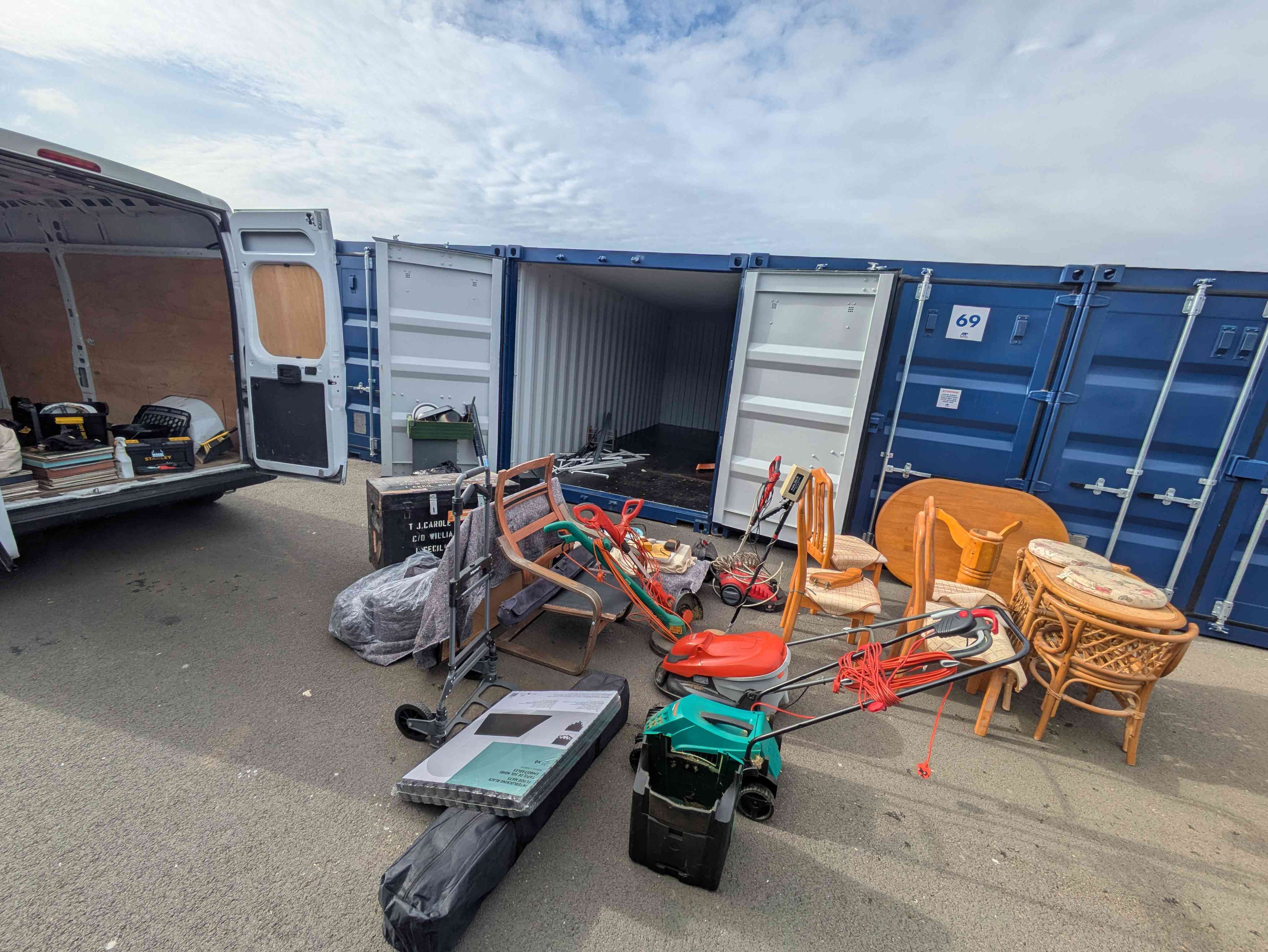 Items laid out on the floor in front of an open storage container — rattan chairs, a router, golf clubs and a folding chair — being triaged