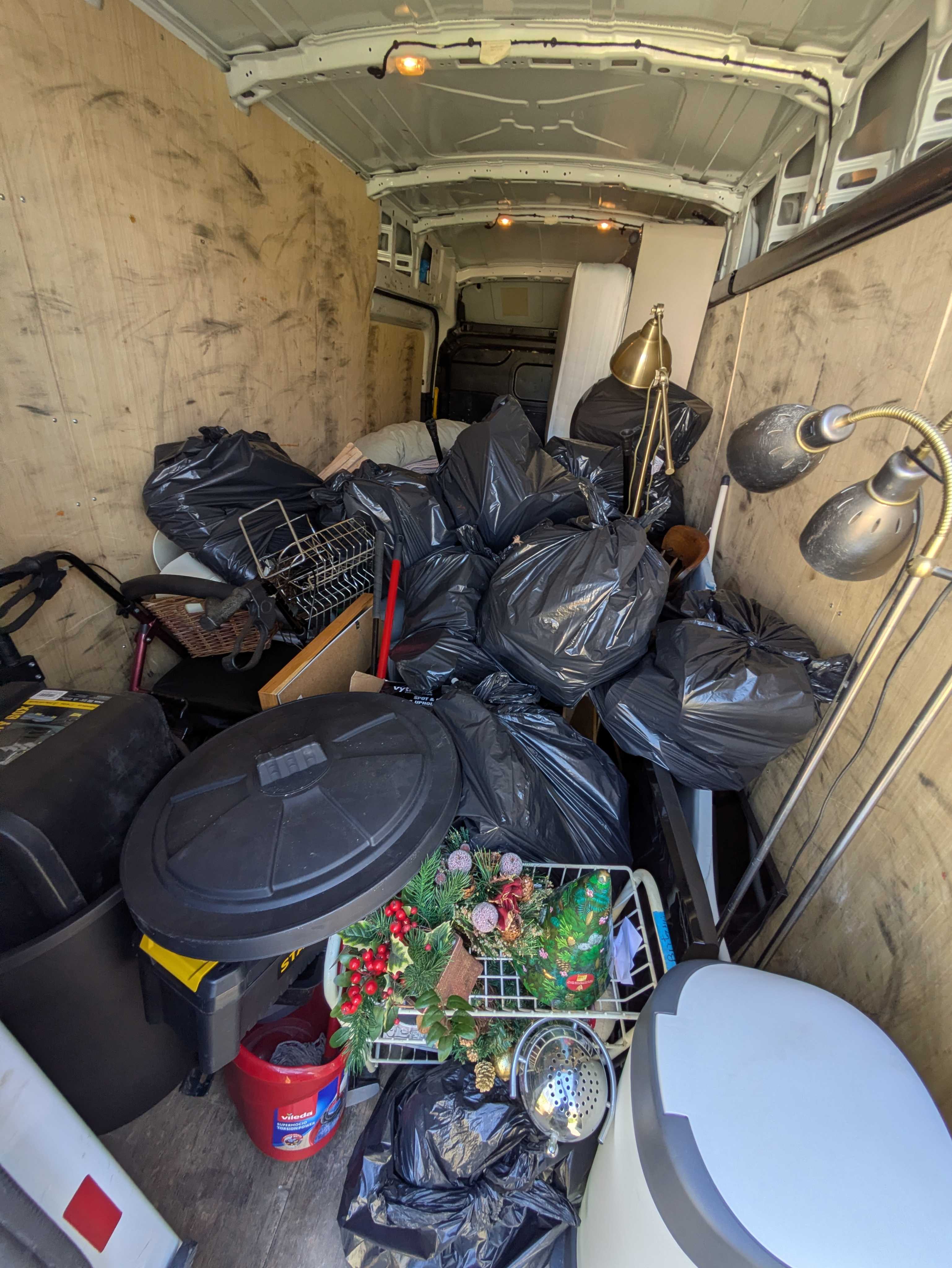 Inside the loaded van at the end of a clearance — bagged waste, a folded table, lamps and a wreath frame neatly stacked floor-to-ceiling