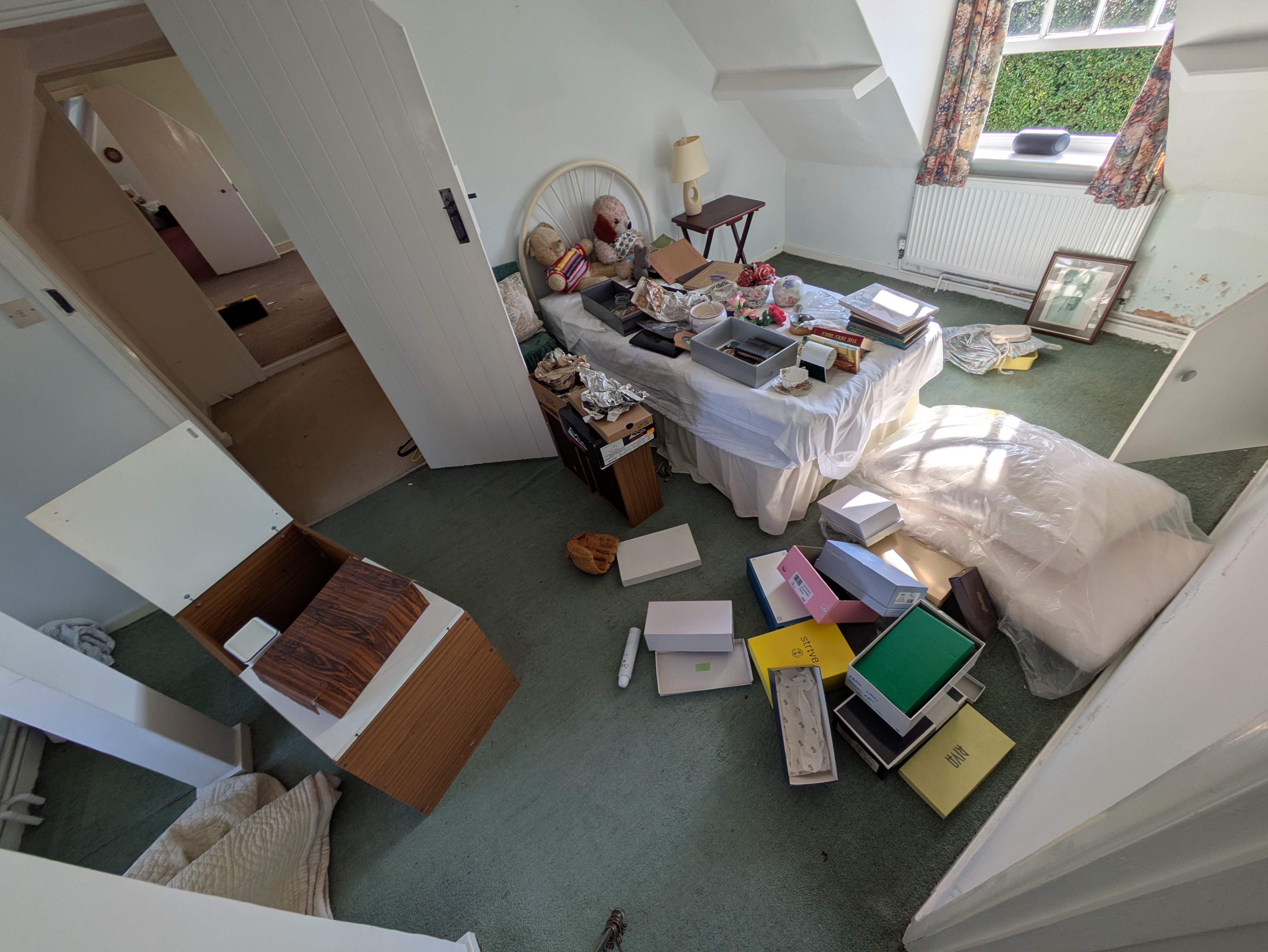 A bedroom in a probate house — bed covered in paperwork and keepsakes, boxes and gift bags strewn across the carpet mid-sort